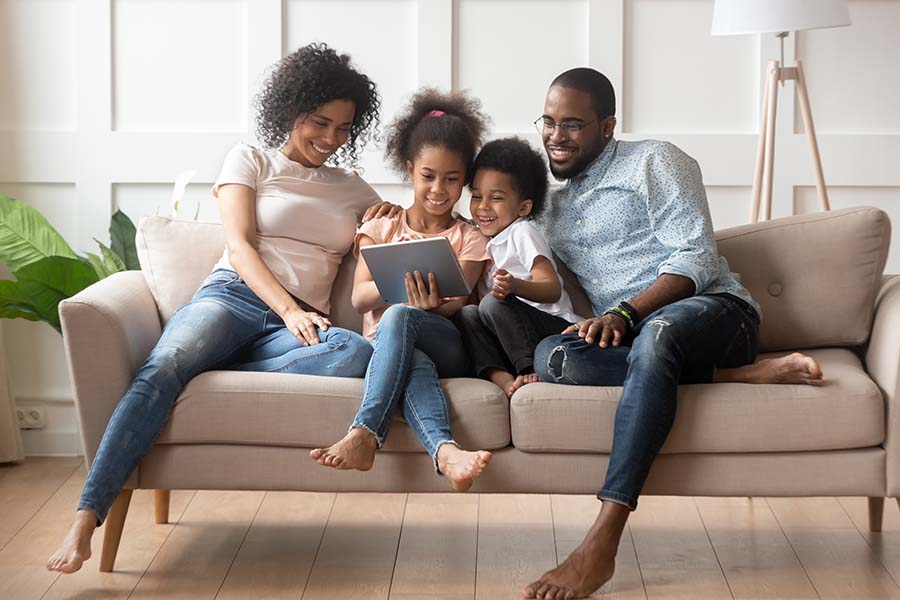 Blog - Portrait of a Smiling Family Sitting on the Couch Enjoying Watching a Video on the Tablet with Their Kids