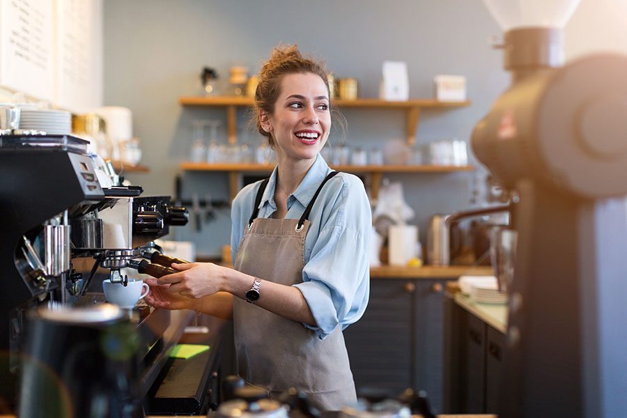 Business Insurance - View of Smiling Business Owner Preparing a Cup of Coffee for a Customer in Her Coffee Shop