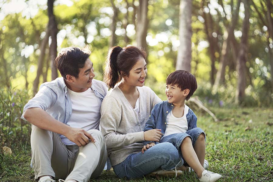 Personal Insurance - Smiling Family with Young Boy Sitting in the Grass in the Countryside Enjoying the Warm Weather